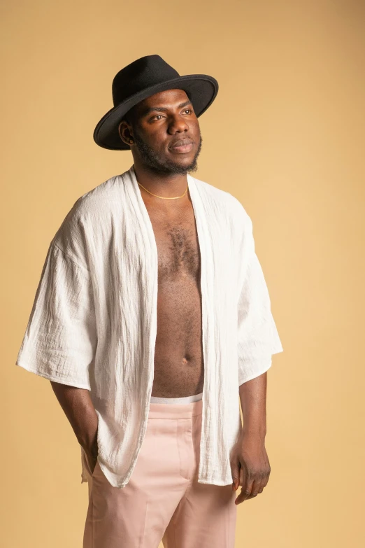 a man in a hat is posing for a picture, an album cover, inspired by Charles Martin, unsplash, figuration libre, dirty linen robes, loin cloth, pale and coloured kimono, samuel l jackson