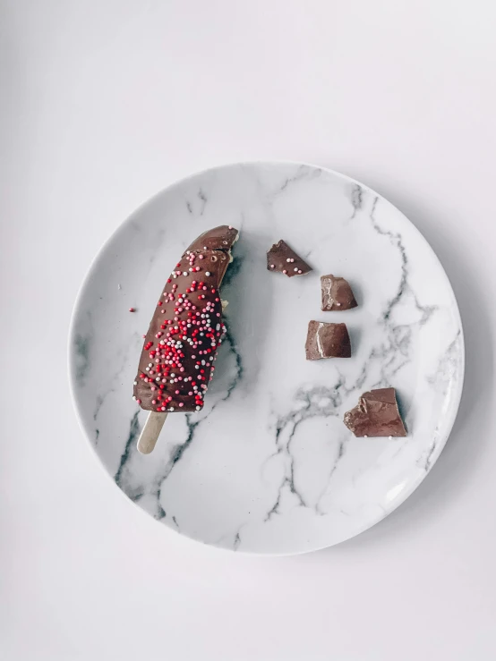 a close up of a plate of food on a table, while marble, fully chocolate, single long stick, 🐿🍸🍋