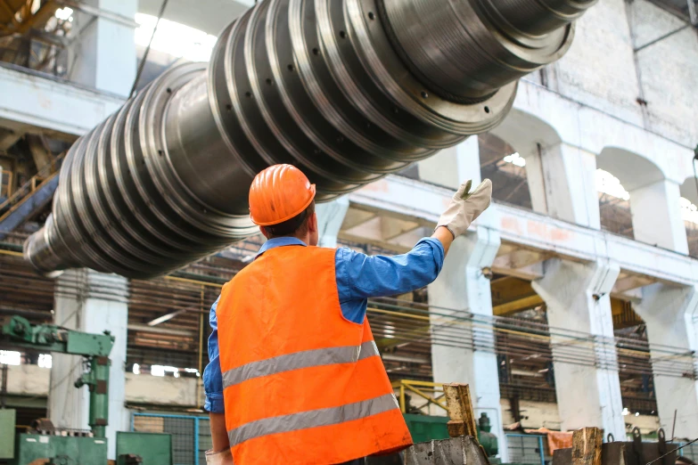 a man in an orange vest holding a large pipe, pexels contest winner, interior of a huge robot factory, turbines, corrugated hose, hydraulics