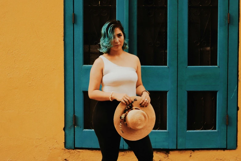 a woman standing in front of a yellow building, inspired by Elsa Bleda, pexels contest winner, wearing sombrero, teal hair, showing curves, dressed in a white t-shirt