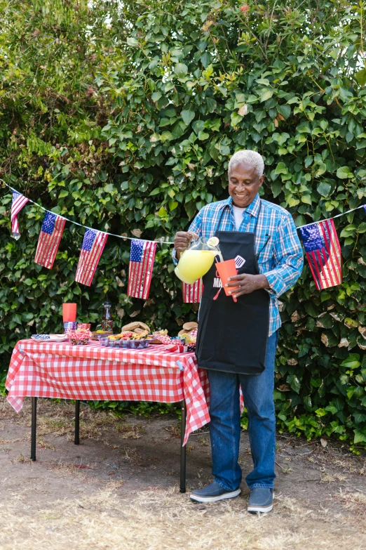 a man standing in front of a table holding a balloon, inspired by Samuel Washington Weis, shutterstock contest winner, apron, american flags, barbecue, mixing drinks