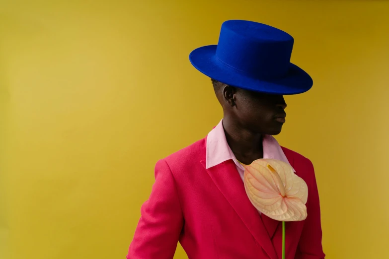 a man in a red suit and blue hat holding a flower, an album cover, inspired by Yves Klein, pexels contest winner, adut akech, pink and yellow, non binary model, shot on hasselblad