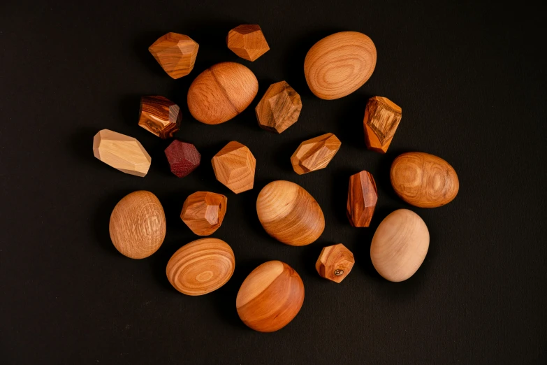 a pile of wooden eggs sitting on top of a black table, inspired by Slava Raškaj, variety of shapes and textures, garnet, cedar, set pieces