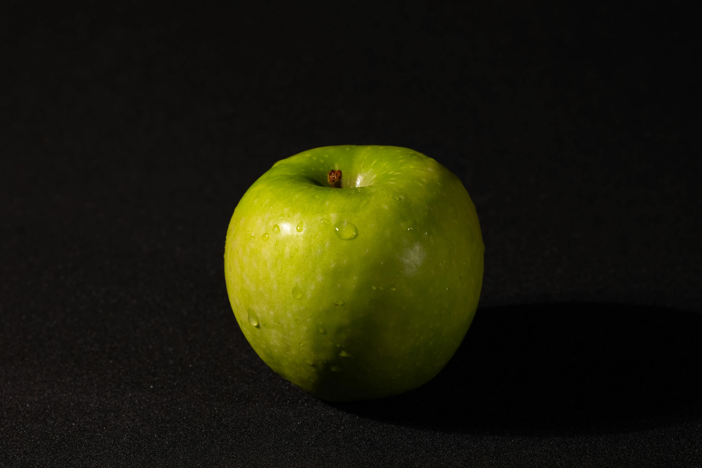 a green apple sitting on top of a black surface, detailed product image, medium angle, fan favorite, ready to eat