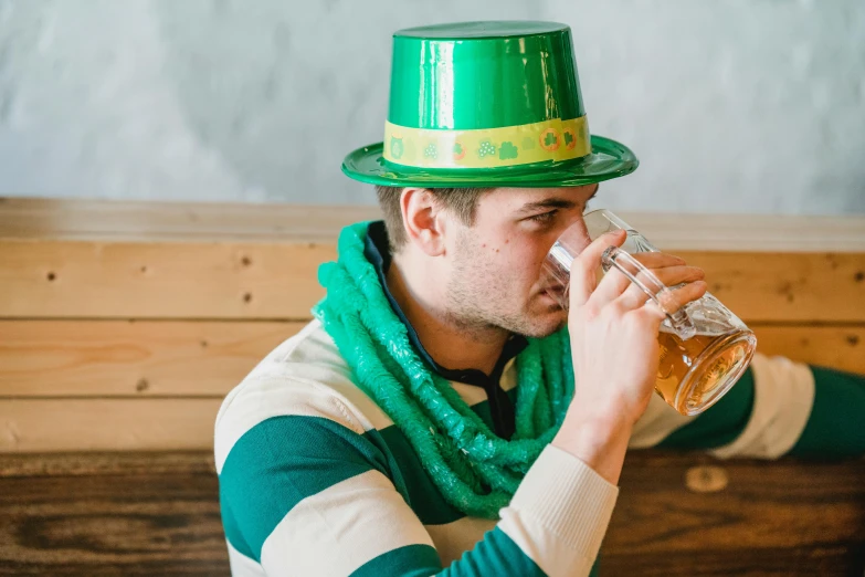 a man in a green hat drinking from a glass, pexels contest winner, irish, costume, ad image, sitting down casually