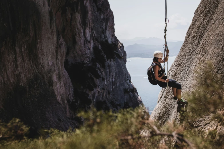 a man hanging from a rope on top of a mountain, rock walls, santorini, high quality product image”