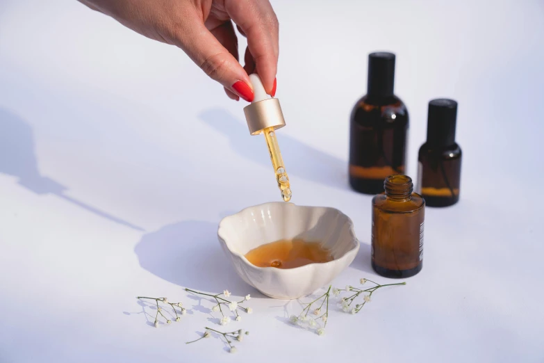 a person pouring syrup into a bowl next to bottles of essential oils, trending on pexels, miniature product photo, half turned around, manicured, angled