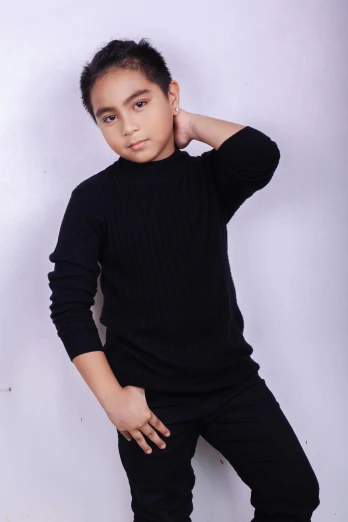 a young boy standing in front of a white wall, an album cover, inspired by Fathi Hassan, pexels contest winner, wearing a black sweater, modeling studio, ((portrait)), modeling for dulce and gabanna