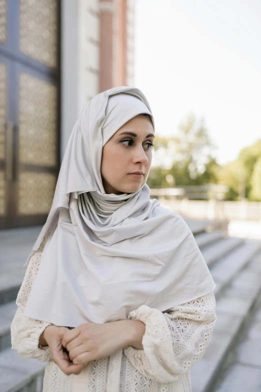 a woman wearing a hijab standing in front of a building, silver，ivory, concerned, curated collections, outdoor photo