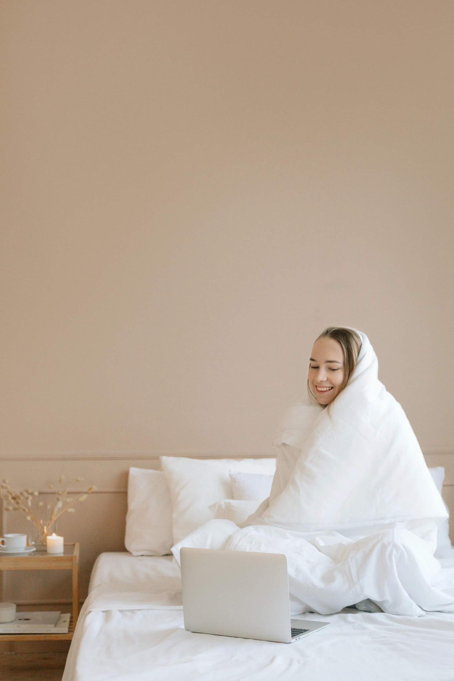 a woman sitting on a bed with a laptop, white cloak, white puffy outfit, wearing a towel, warm and happy