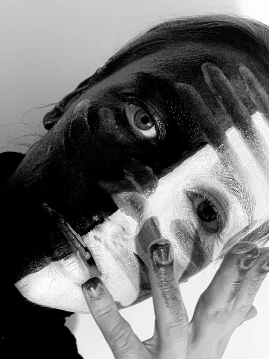 a woman with black and white paint on her face, a black and white photo, pexels contest winner, surrealism, close-up!!!!!!, man is with black skin, hands shielding face, painting a self portrait