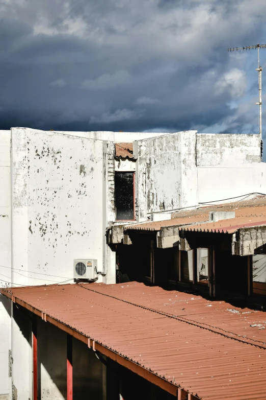 a white building with a red roof under a cloudy sky, by Alejandro Obregón, quito school, battle damage, an old cinema, puerto rico, in a rooftop