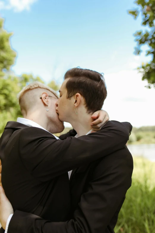 a couple of men standing next to each other, unsplash, romanticism, kissing each other, trees in background, shaven, grand finale