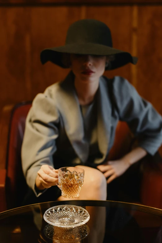 a woman sitting at a table with a glass of wine, van cleef & arpels style, tipping his fedora, amber, cinematic shot ar 9:16 -n 6 -g