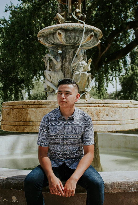 a man sitting on a bench in front of a fountain, an album cover, inspired by Eddie Mendoza, patterned clothing, justin sun, yearbook photo, looking straight to camera