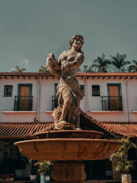 a statue on top of a fountain in front of a building, by Alejandro Obregón, pexels contest winner, the city of santa barbara, village square, mid-shot of a hunky, exterior