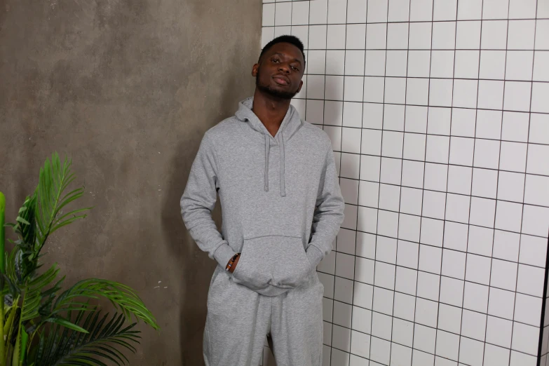 a man standing in front of a tiled wall, instagram, wearing a grey hooded sweatshirt, david uzochukwu, wearing track and field suit, on a pale background