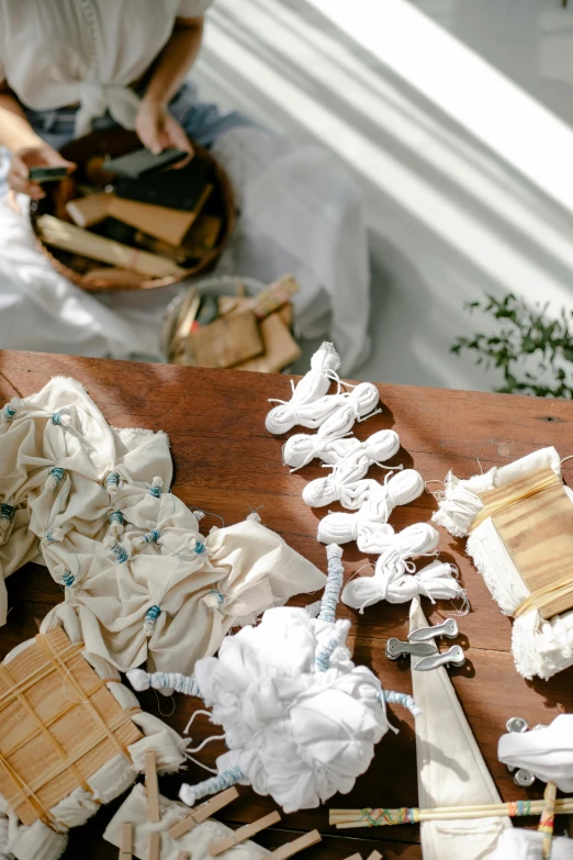 a woman sitting on top of a wooden table, a still life, by Jessie Algie, unsplash, process art, laces and ribbons, white ceramic shapes, displayed on an altar, close-up from above