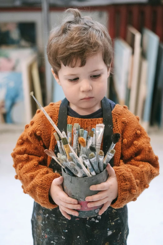 a young boy holding a bucket full of paint brushes, inspired by Kyffin Williams, pexels contest winner, portrait of a small, handcrafted, portrait of small