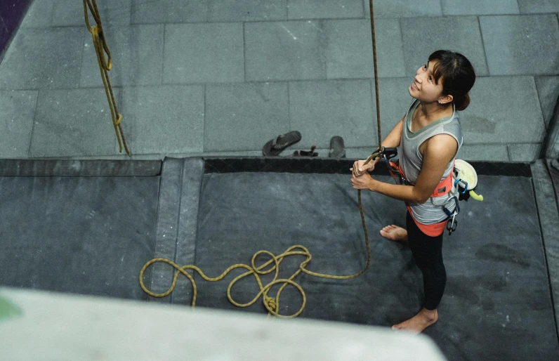 a woman on a climbing wall holding a rope, a portrait, pexels contest winner, looking down from above, asian woman, inside building, promo image