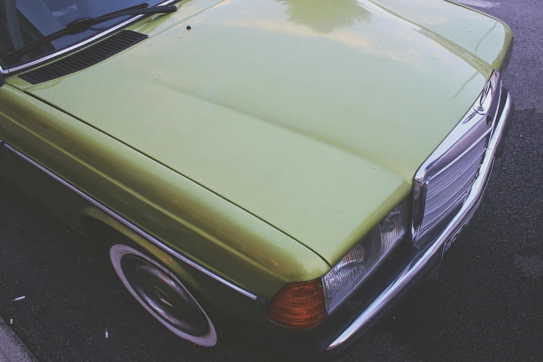 a green car parked on the side of the road, inspired by Elsa Bleda, pexels contest winner, photorealism, 7 0 s palette, greenish skin, yellow, mercedes