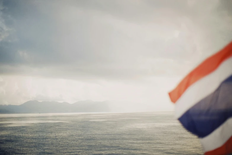 a red, white and blue flag flying over a body of water, a picture, inspired by Francisco de Holanda, unsplash, dutch, south african coast, looking across the shoulder, on a yacht at sea