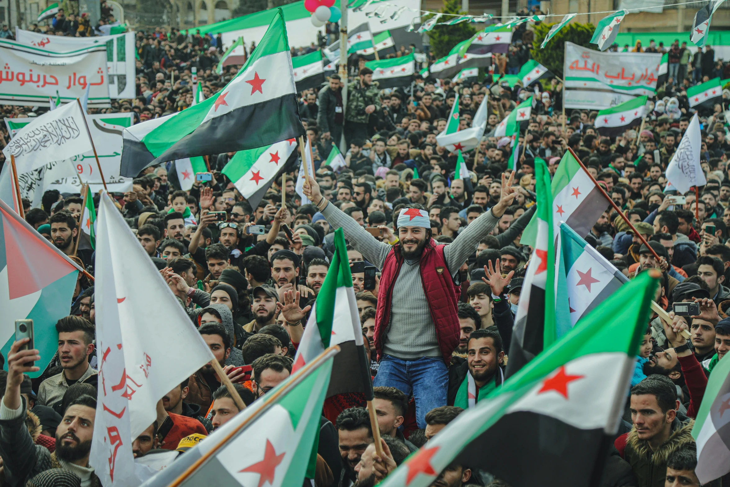 a large crowd of people holding flags and banners, a cartoon, trending on unsplash, hurufiyya, real life photo of a syrian man, square, a green, january 20th