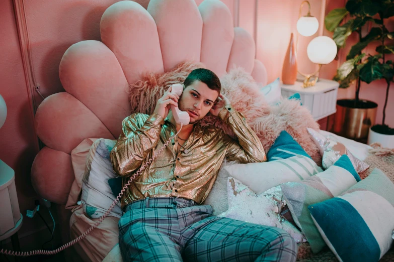 a man sitting on a bed talking on a phone, an album cover, inspired by Elsa Bleda, trending on pexels, maximalism, gold suit, melanie martinez, zachary quinto, brightly lit pink room