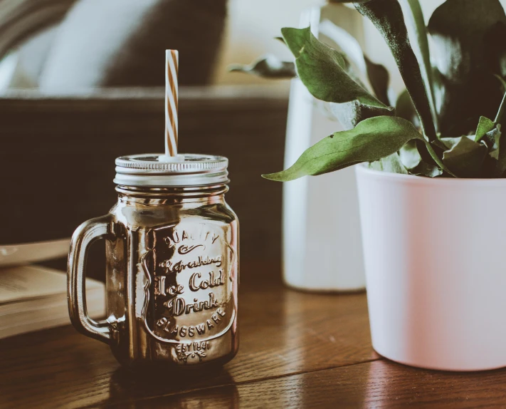 a mason jar sitting on a table next to a plant, unsplash, milkshake, engraved, brown, shiny silver