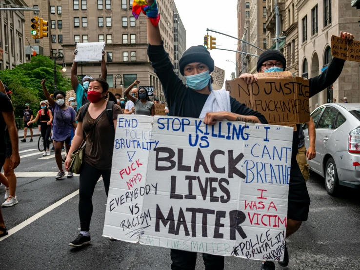 a group of people walking down a street holding signs, a photo, pexels, black arts movement, a person standing in front of a, nypd, a colorful, black bandage on arms
