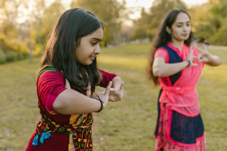 a couple of women standing on top of a lush green field, an album cover, pexels contest winner, hurufiyya, anjali mudra, kids playing, gracefully belly dancing pose, at a park