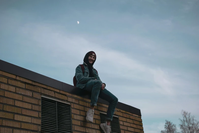 a man sitting on top of a brick building, by Niko Henrichon, pexels contest winner, girl wearing hoodie, the moon cast on the man, smiling, lil peep