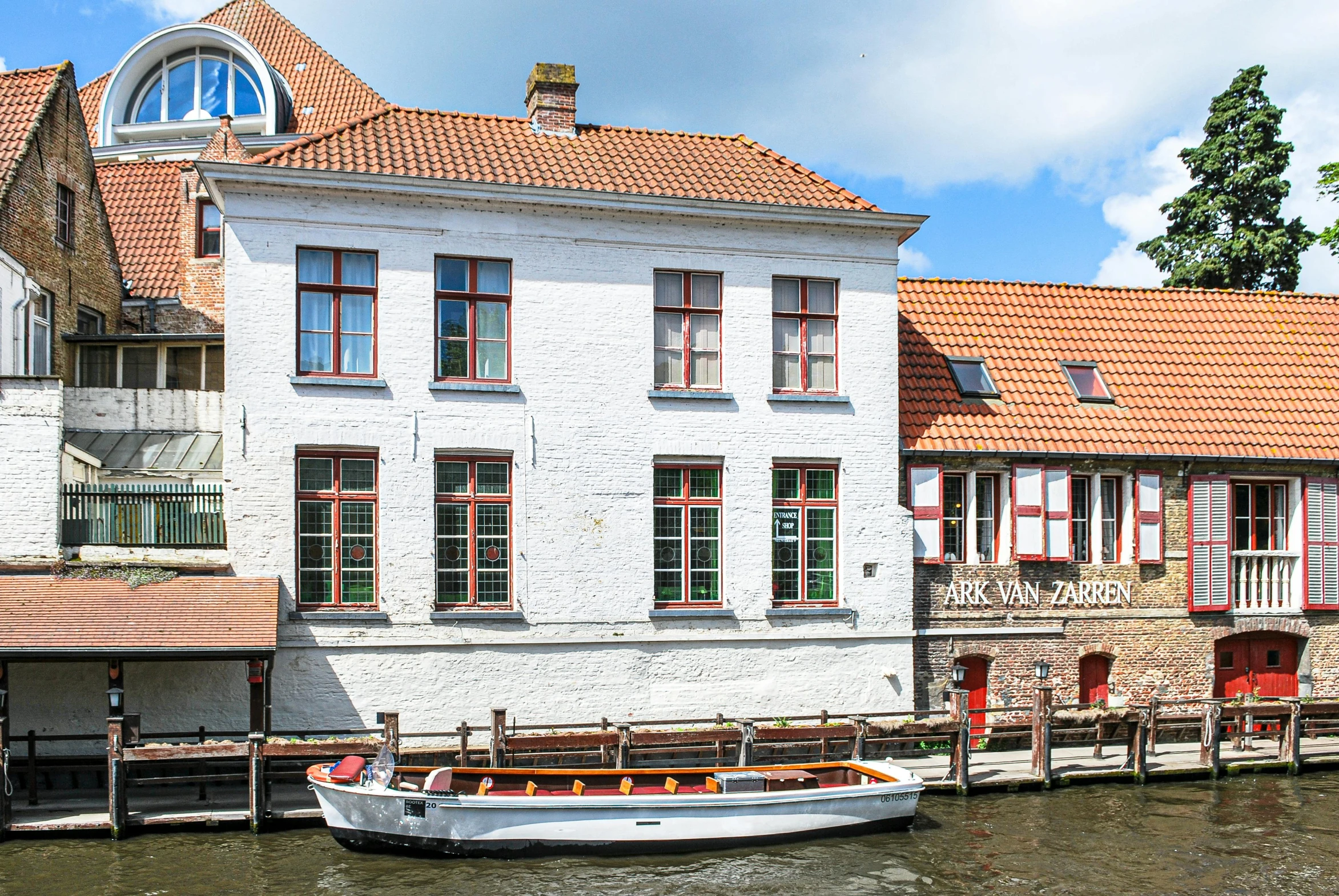 a boat sitting on top of a river next to a building, by Jan Tengnagel, white buildings with red roofs, well preserved, as photograph