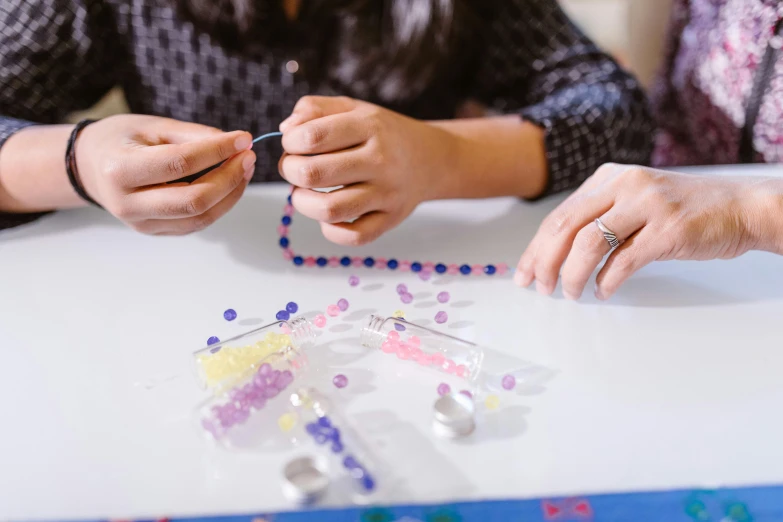 a couple of people that are sitting at a table, a cross stitch, trending on pexels, glass beads, purple themed, made of plastic, teenage girl