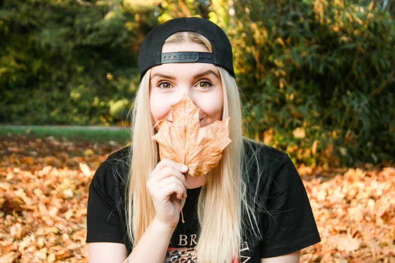 a woman holding a leaf in front of her face, pexels contest winner, wearing a black t-shirt, ricky berwick, blonde women, 🍂 cute