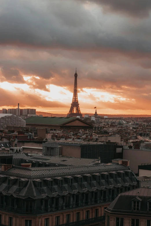 a view of the eiffel tower from the top of a building, sunset with cloudy skies, on a rooftop