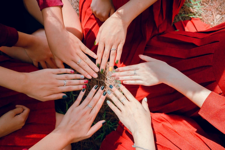 a group of people with their hands in a circle, a photo, by Julia Pishtar, trending on pexels, aestheticism, red robes, chaumet, sustainable materials, painted nails