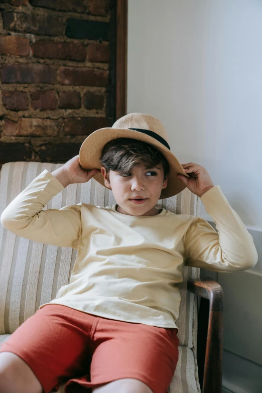 a young boy sitting in a chair wearing a hat, inspired by Henri de Toulouse-Lautrec, pexels contest winner, renaissance, wear's beige shirt, wearing casual clothing, beams, curated collections