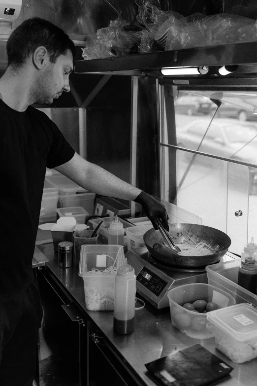 a man standing in a kitchen preparing food, a black and white photo, unsplash, food stall, square, hot food, 2708519935