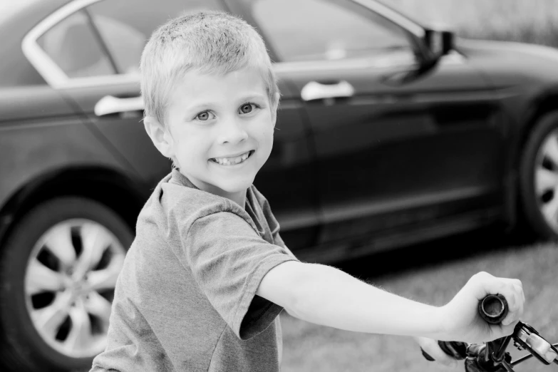 a young boy riding a bike in front of a car, a black and white photo, by Matt Cavotta, pixabay contest winner, smiling playfully, avatar image, holding a whip, connor hibbs