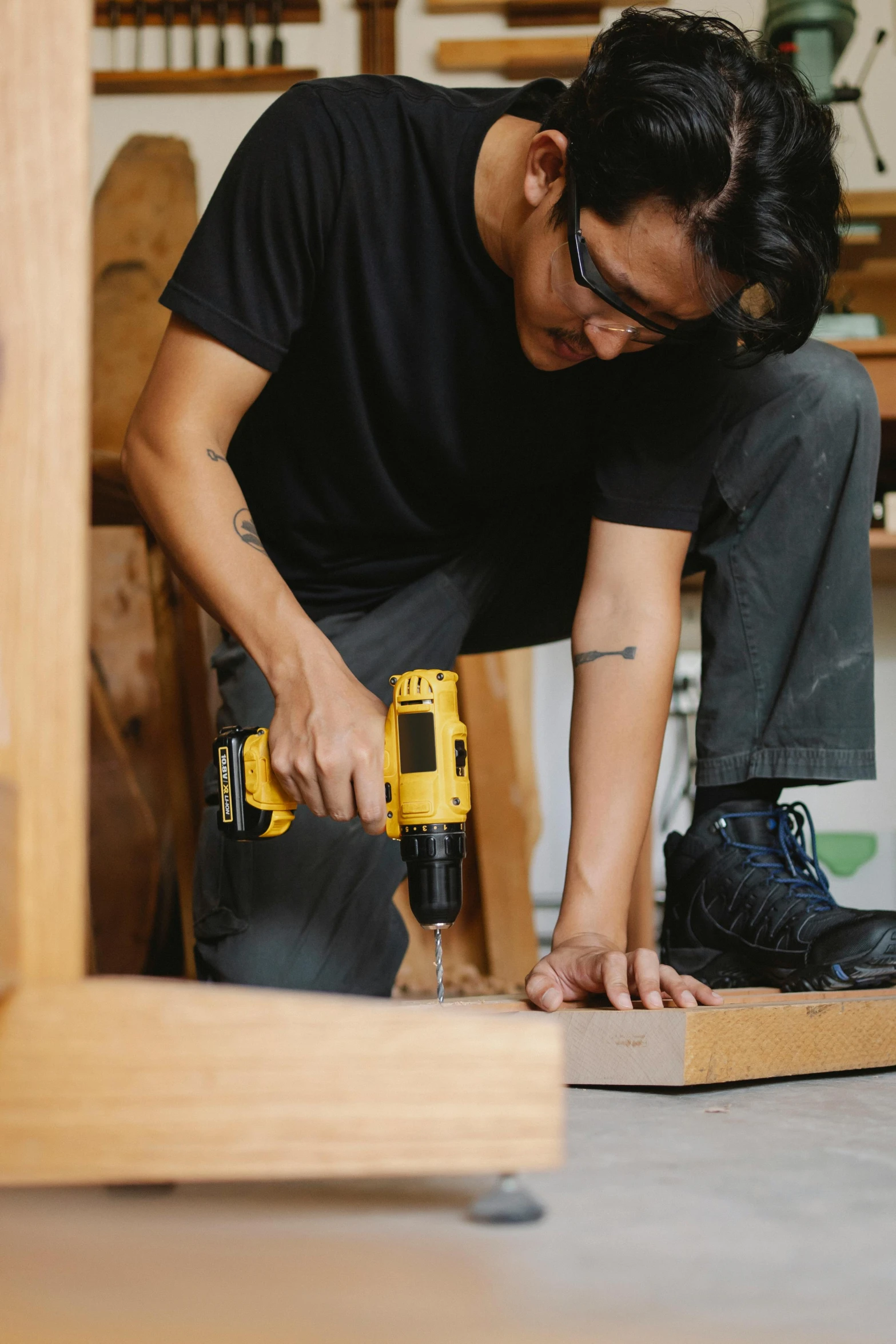 a man using a power drill on a piece of wood, by Everett Warner, pexels contest winner, asian male, yellow and black color scheme, standing on a desk, heavy-duty boots