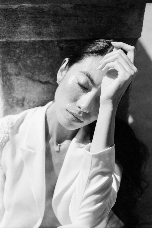 a black and white photo of a woman leaning against a wall, inspired by Max Dupain, unsplash, shin hanga, wearing white suit, maggie cheung, an exhausted deity, sun lighting