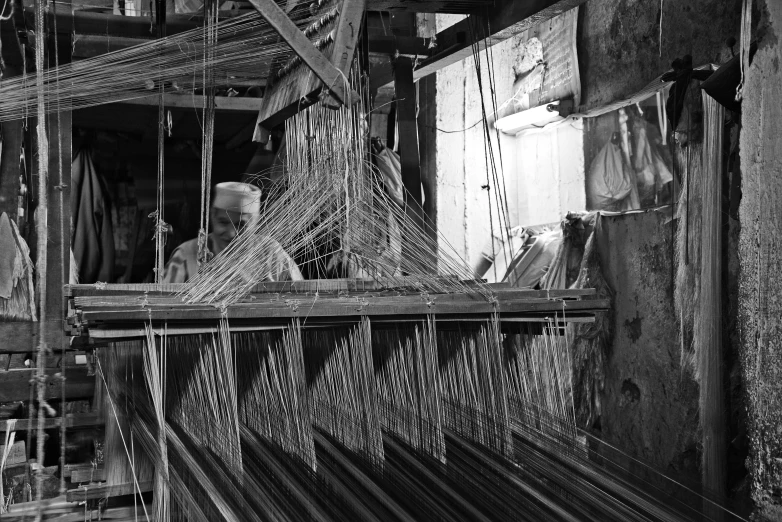 a black and white photo of a man working on a loom, by Sudip Roy, ffffound, tri - x pan stock, around the city, bamboo