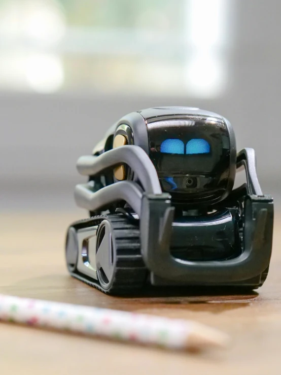 a toy robot sitting on top of a table next to a pencil, front facing the camera, a robot, zoomed in