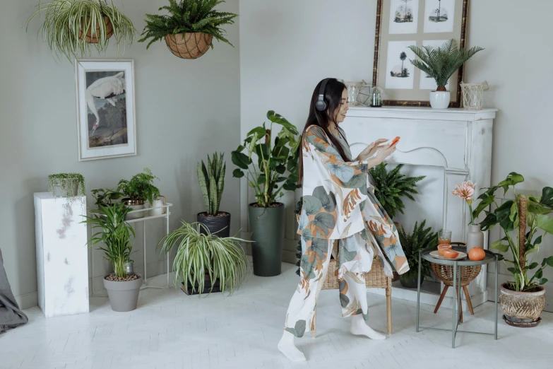 a woman standing in a living room next to a fireplace, inspired by Tani Bunchō, trending on pexels, arts and crafts movement, waving robe movement, woman made of plants, karate outfit, listening to music