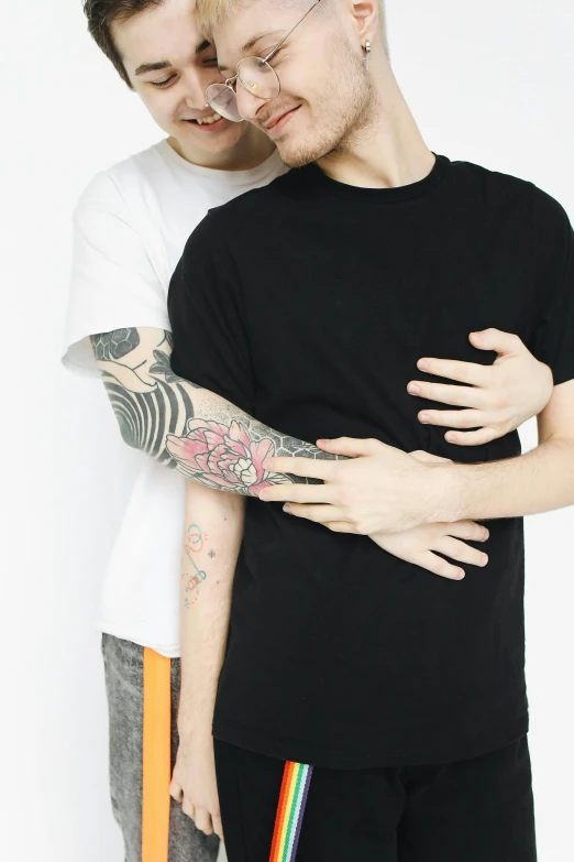 a man and a woman standing next to each other, a tattoo, trending on pexels, antipodeans, two men hugging, wearing a black t-shirt, non binary model, white bg