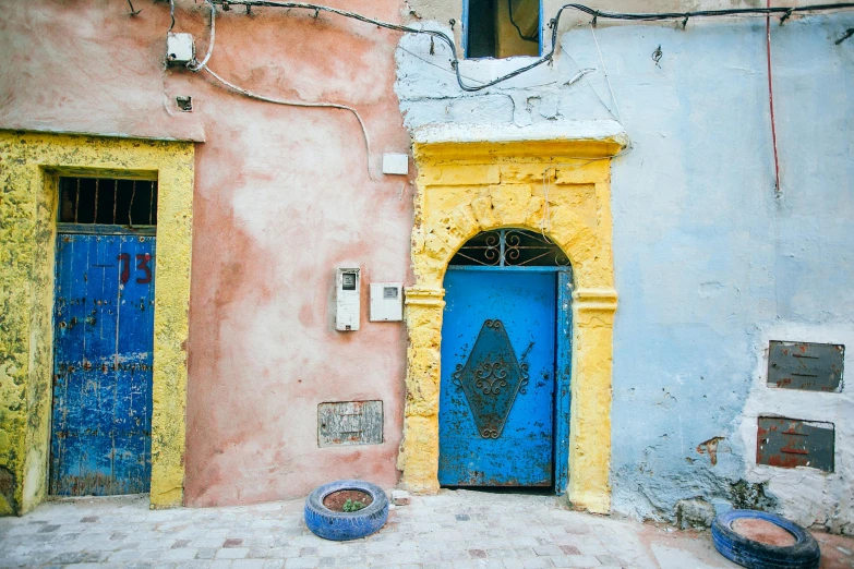 a blue door sitting on the side of a building, inspired by Alberto Morrocco, pexels contest winner, les nabis, turquoise pink and yellow, mud and brick houses, with an intricate, moroccan