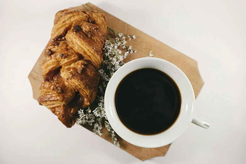 a croissant next to a cup of coffee, unsplash, black and brown, vine twist, on a wooden tray, white