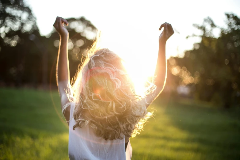a woman standing on top of a lush green field, pexels, happening, flowing backlit hair, sparkling in the sunlight, a blond, cheering