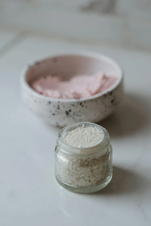 a white bowl sitting on top of a counter next to a pink bowl, stone dust, detailed product image, jars, mask